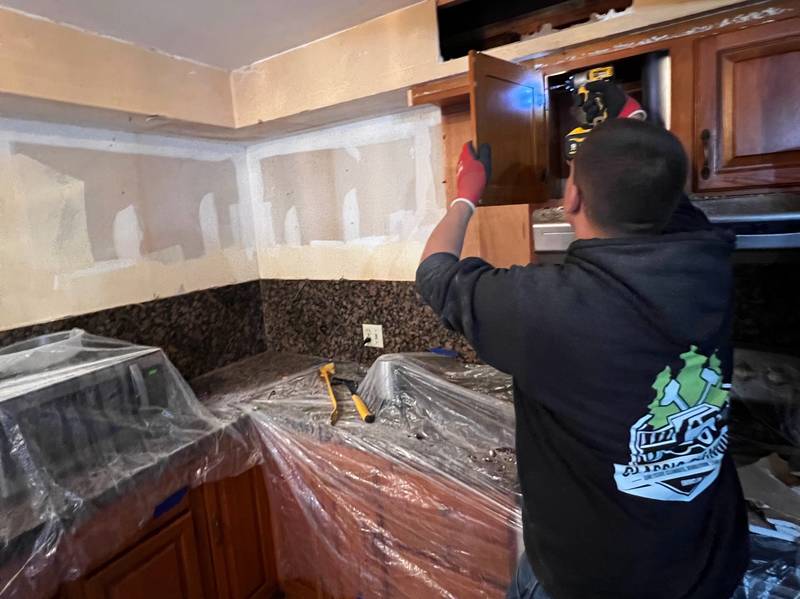 Classic Cleanouts crew member removing kitchen cabinets with counters and appliances covered in plastic during a light demolition job